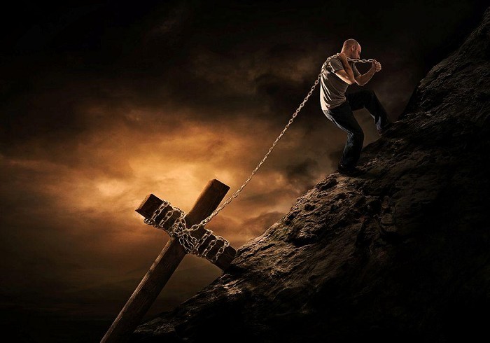 A man is carrying his cross up a mountain.